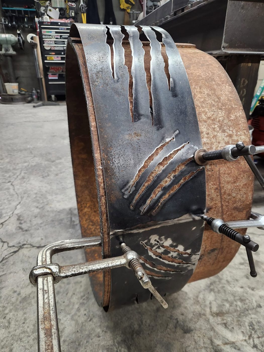 Steel band with plasma-cut claw marks clamped to the rusted tank body