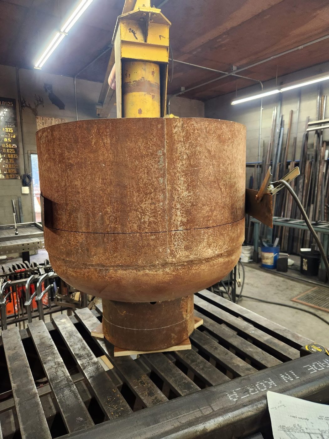 Rusted propane tank with cut lines scribed around it, set on a steel welding table