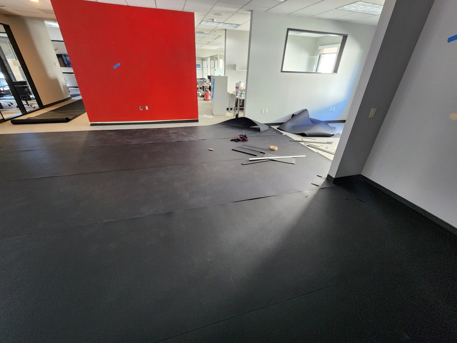 Rubber flooring seams taped and cut-off scraps staged mid-installation in a Saratoga office