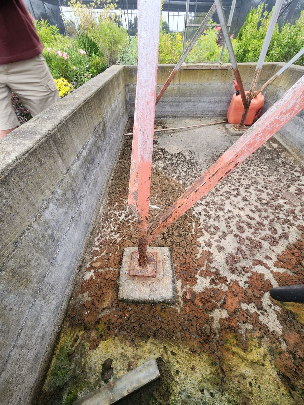 Close-up of a rusted angle-iron post base on a diesel tank stand