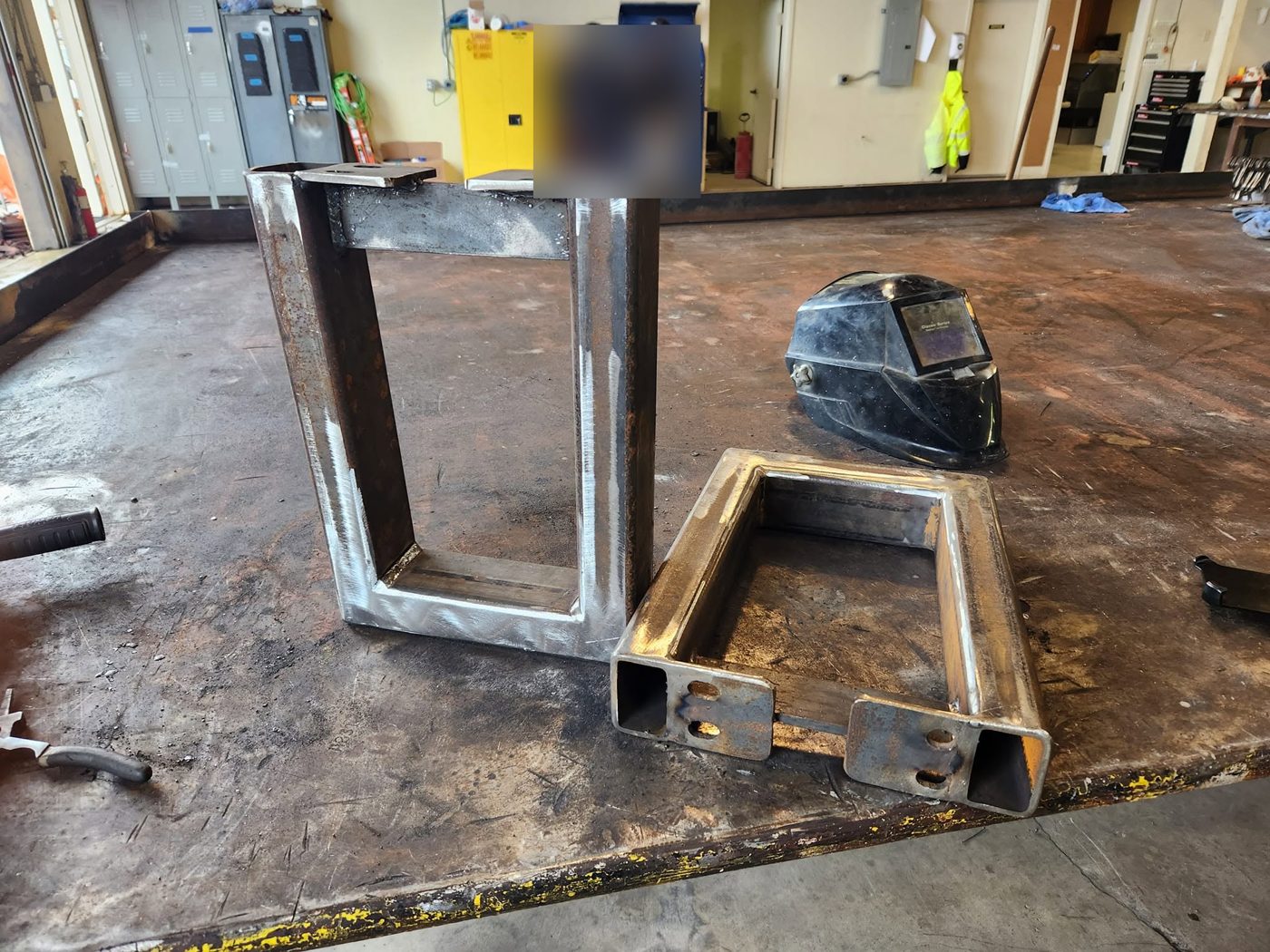 Two raw welded steel bench legs on the table before priming