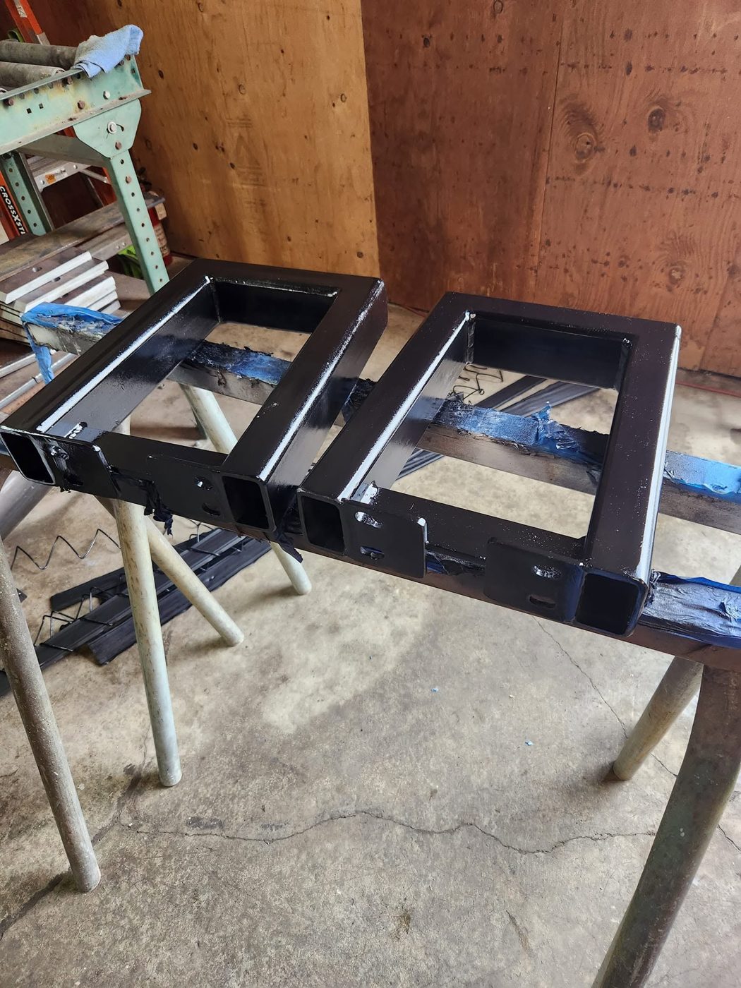 Two new welded steel bench legs, primed and painted black, sitting on jacks